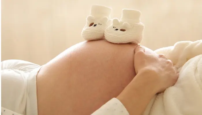 赤ちゃん用の靴をお腹に乗せ横たわっている妊婦