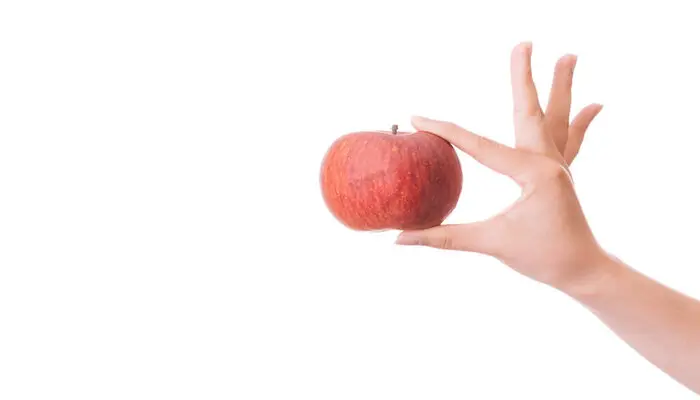 親指と人差し指でリンゴをつまみかざしている手