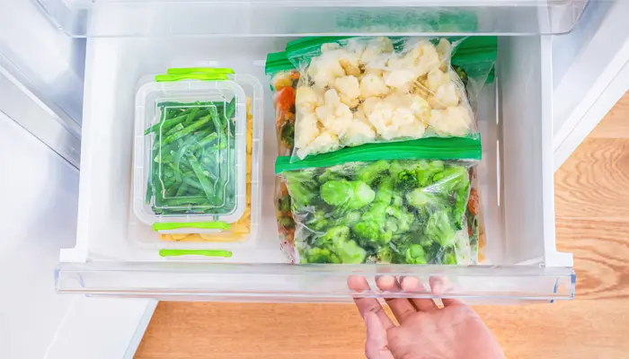 保存容器に入った野菜が入っている冷凍庫を開けている人の手