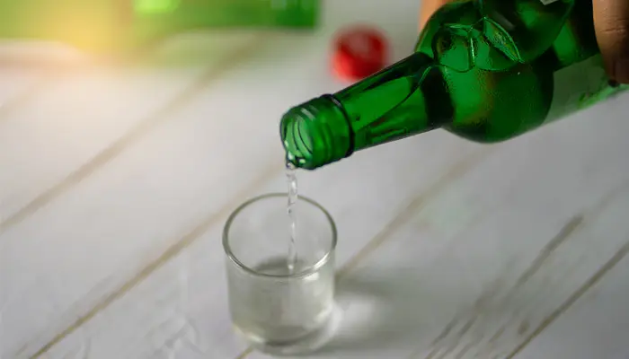 緑の瓶からおちょこにお酒を注いでいる