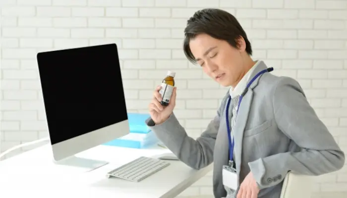 パソコンの前に座り栄養ドリンクを手に持つ男性